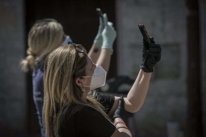 Dos personas protegidas con mascarillas y guantes graban con sus móviles  durante el estado de alarma en Sevilla