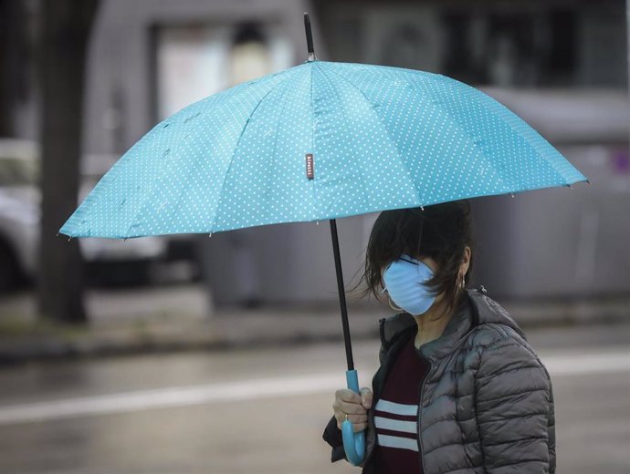 Una mujer protegida con mascarilla y guantes se resguarda de la lluvia bajo su paragüas en la quinta semana del estado de alarma por el coronavirus, Covid-19. En Sevilla (Andalucía, España), a 15 de abril 2020.