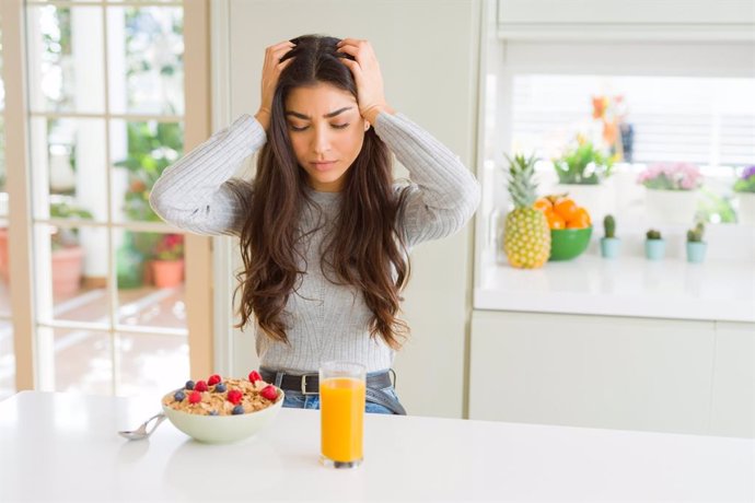 Joven desayunando con dolor de cabeza, migraña, cefalea.