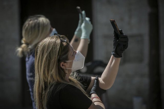 Dos personas protegidas con mascarillas y guantes en Sevilla graban con sus móviles durante el Estado de Alarma