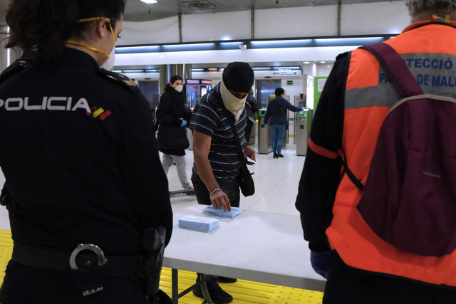 Un joven recoge una de las mascarillas puestas a disposición de viajeros y usuarios de transporte público en las inmediaciones de la estación Intermodal.