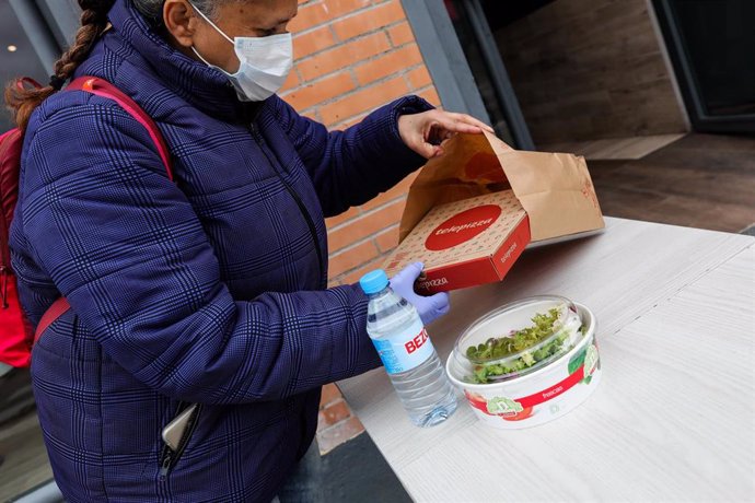 Una mujer protegida con mascarilla y guantes de látex abre el menú infantil de Telepizza en el barrio de San Fermín en el distrito de Usera.