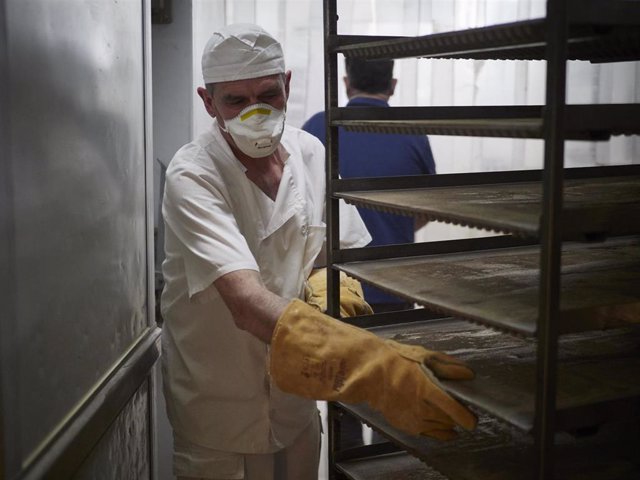 Un trabajador protegido con mascarilla maneja bandejas para cocer pan en el obrador panadería