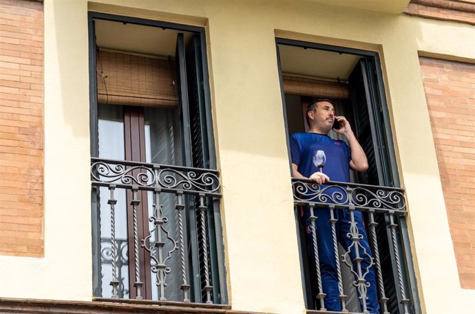 Un vecino de Triana asomado al balcón de su casa con una copa de vino  el día 34 del estado de alarma. Sevilla a 17 de abril del 2020
