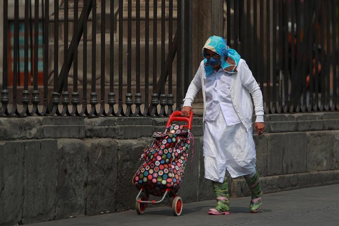 Una mujer con mascarilla y bata en una calle de México.