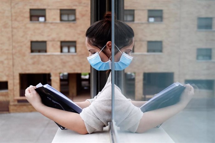 Una mujer con una mascarilla lee asomada a la ventana de su casa durante el confinamiento por el coronavirus, en Valdemoro/Madrid (España) a 20 de abril de 2020.