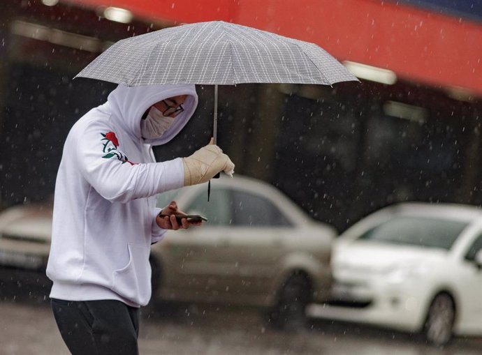 Transeúntes protegidos con mascarilla y un paraguas caminan por las calles de la capital un día marcado por la llegada a la península de una borrasca fría que ha activado la alerta por viento o lluvia en 8 comunidades, entre ellas, Madrid, en los inicio