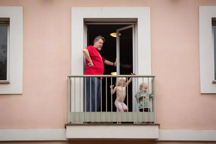Un home i els seus dos fills petits treuen el cap a la balconada durant el segon dia laborable de l'estat d'alarma pel coronavirus, a Barcelona/Catalunya (Espanya), a 17 de mar de 2020.