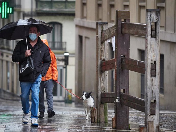 Un hombre con mascarilla camina bajo la lluvia junto al vallado permanente del encierro de Pamplona.