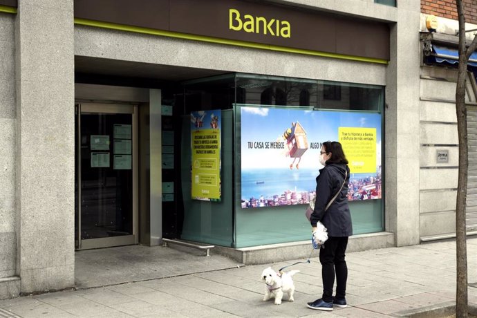Una mujer pasea con un perro frente a una sucursal de Bankia un día después de que Banco Central Europeo (BCE) haya especificado que decidirá "banco a banco" la hoja de ruta para recuperar los niveles de capital y liquidez previos a la crisis generada p
