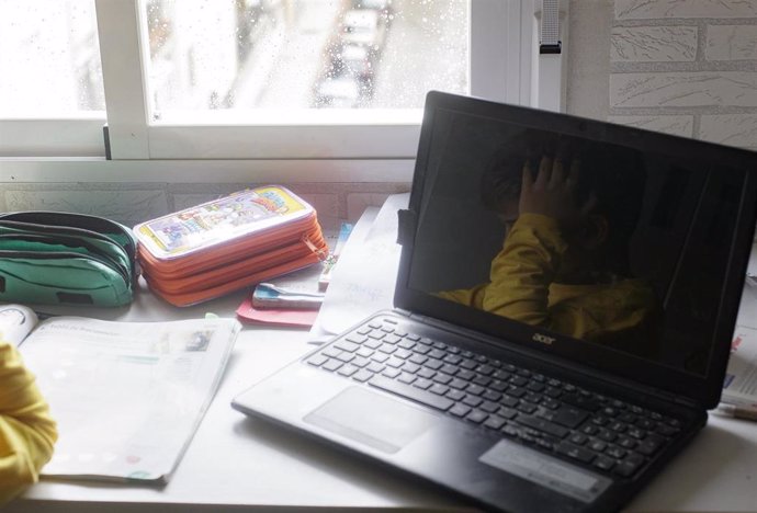 Reflejo en un ordenador portátil de un niño estudiando y haciendo los deberes en casa, foto de archivo