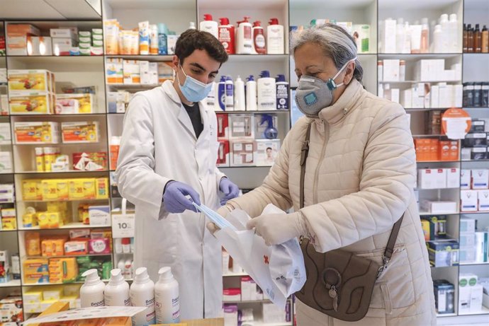 Un farmacéutico da una mascarilla a una mujer durante el reparto de mascarillas gratuitas contra el Covid-19 a mayores de 65 años y colectivos de riesgo que ayer arrancó en la Comunitat Valenciana. En Valencia (España) a 21 de abril de 2020.