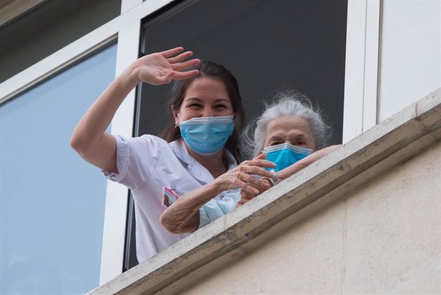 Una sanitaria ayuda a una paciente mayor a salir a la ventana para rendir homenaje a los sanitarios en el Hospital Fundación Jimenez Diaz 