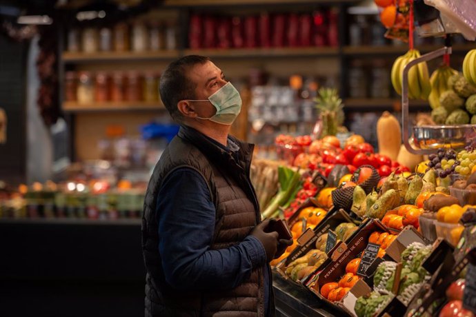 Un home protegit amb mascarilla és ats en una frutería durant el segon dia laborable de l'estat d'alarma pel coronavirus, a Barcelona (Espanya), a 17 de mar de 2020.