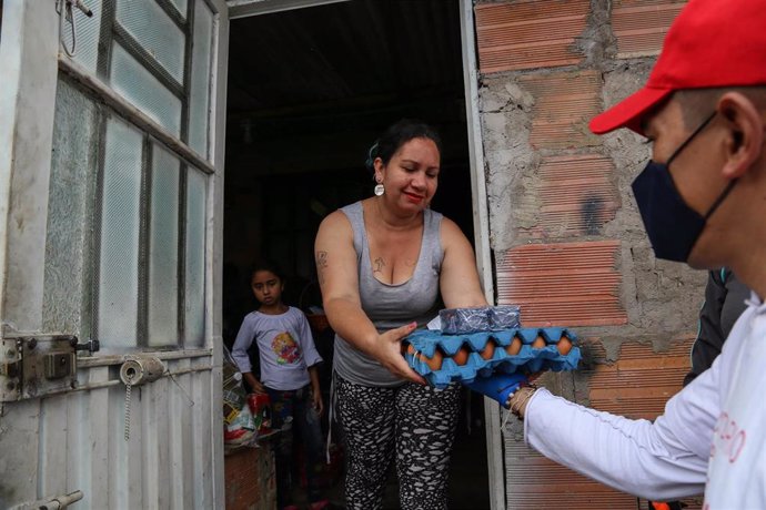 Un miembro de la Policía Militar entrega alimentos a una mujer durante un toque de queda impuesto para combatir la propagación del coronavirus en Bogotá, Colombia.
