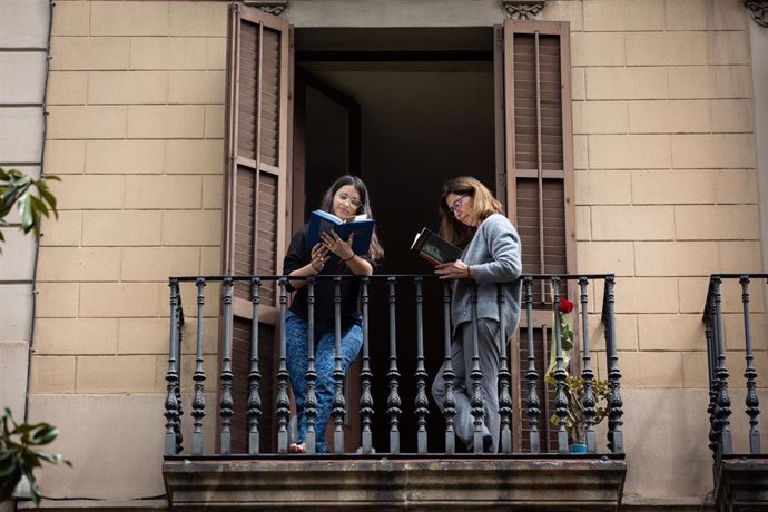 Dos joves llegeixen en la balconada de la seva casa en ocasió de la Diada de Sant Jordi, en la qual és costum regalar llibres i roses, a Barcelona / Catalunya (Espanya), a 23 d'abril de 2020.