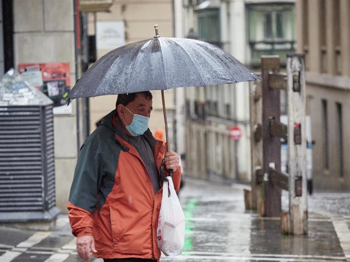 Un hombre con mascarilla camina bajo la lluvia junto al vallado permanente del encierro de Pamplona de la cuesta de Santo Domingo, el mismo día en el que el Ayuntamiento de Pamplona ha decidido suspender la celebración de las fiestas de San Fermín este 