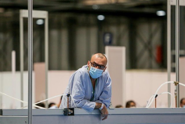 Un paciente se asoma por encima de una mampara durante la lectura de pasajes de ‘El Quijote’ para los sanitarios y pacientes del Hospital temporal de IFEMA para enfermos con Covid-19.