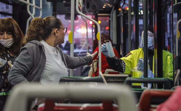 Un policía local de Valencia entrega una mascarilla a una mujer dentro de un autobús urbano