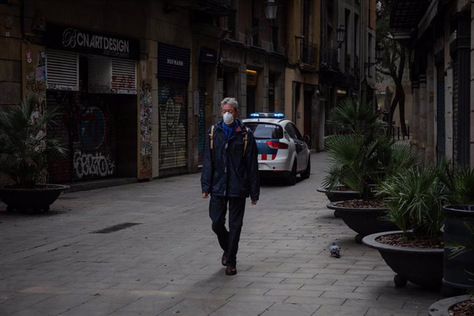 Un hombre con mascarilla pasea por una calle de Barcelona junto a un coche de la Policía en el segundo día laborable del estado de alarma por el coronavirus, en Barcelona (España), a 17 de marzo de 2020.