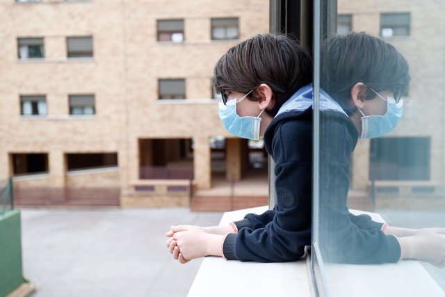 Un niño con una mascarilla se asoma a la ventana de su casa, en Valdemoro - Madrid a 20 de abril de 2020