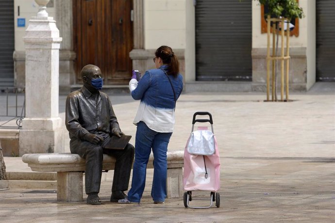 Una mujer toma una foto de una estatua con mascarilla.
