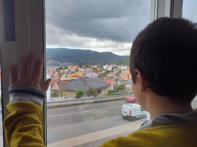 Un niño observa la calle desde el interior de su casa.