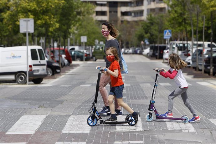 Dos niñas con mascarillas cruzan un paso de cebra montadas en patinete tras salir a la calle el primer día en el que los menores de 14 años lo pueden hacer durante el estado de alarma, en Palma de Mallorca/Islas Baleares (España) a 26 de abril de 2020.