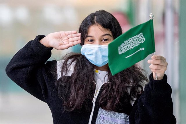 Una muchacha posa sosteniendo una bandera de Arabia Saudí en el aeropuerto de Riad.