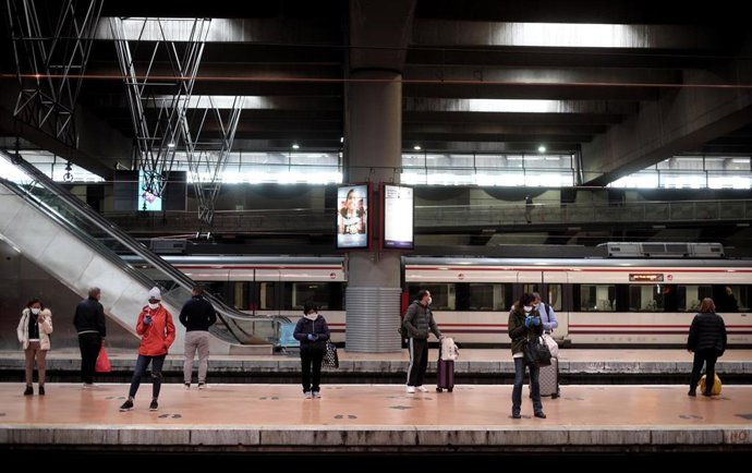 Viajeros esperan en uno de los andenes de Atocha donde la policía está entregando mascarillas a los usuarios de transporte público 