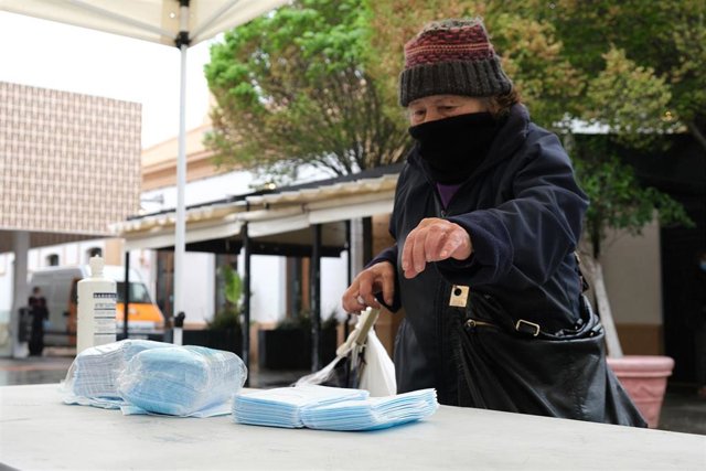 Transeúntes recogen mascarillas puestas a disposición de viajeros y usuarios de transporte público en las inmediaciones de la estación Intermodal de Palma de Mallorca 