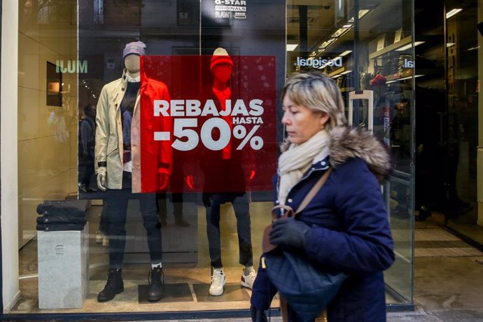 Una mujer pasea junto a una tienda de ropa en Madrid, en la que se ofertan rebajas de hasta el 50%.