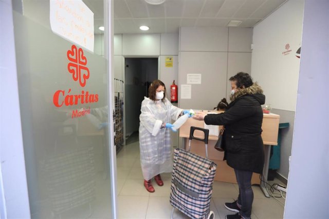 Una voluntaria hace cumplir a una mujer las normas de higiene en un economato solidario de Cáritas 