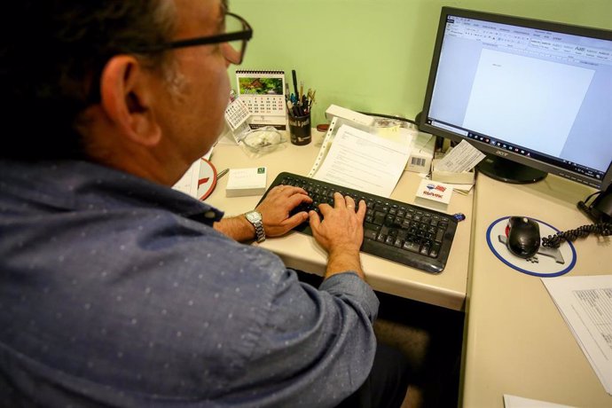 Un hombre escribe con el teclado de su ordenador, mientras trabaja en el despacho de su oficina.