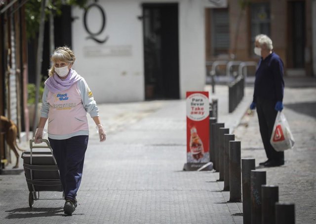 Una mujer con mascarilla, guantes y un carrito de la compra camina por el barrio de la Alameda, durante el día 38 del estado de alarma en el país por la crisis del coronavirus. En Sevilla (Andalucía, España), a 21 de abril de 2020.