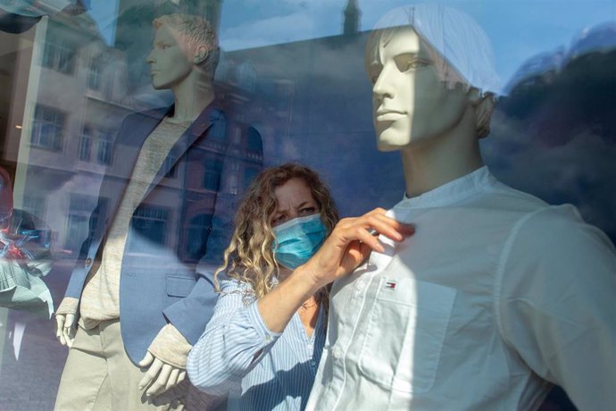 Dorothee Hahn, a visual marketing designer for the Ramelow fashion house, wears a face mask as she dresses a Mannequin. Most of the shops across the country had been closed in recent weeks due to the nationwide spread of the coronavirus.