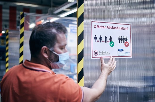 Un empleado de Ford colocando un cartel que pide distanciamiento entre los trabajadores para evitar contagios.