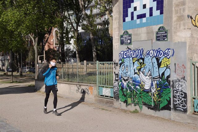 Un hombre con mascarilla junto a un graffitti de coronavirus en París