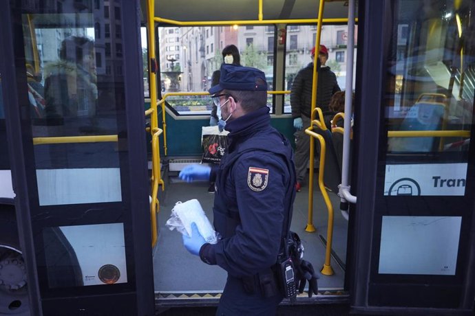 Un policía nacional entrega mascarillas a los pasajeros de un autobús urbano urbano de Pamplona el día en el que se reactiva la actividad laboral no esencial en Navarra en las empresas cuyos empleados no puedan teletrabajar cuando se cumple un mes desde