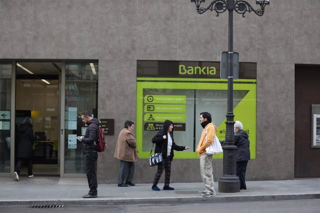Varias personas esperan en una cola respectando la distancia de seguridad para entrar en una sucursal de Bankia de Madrid 