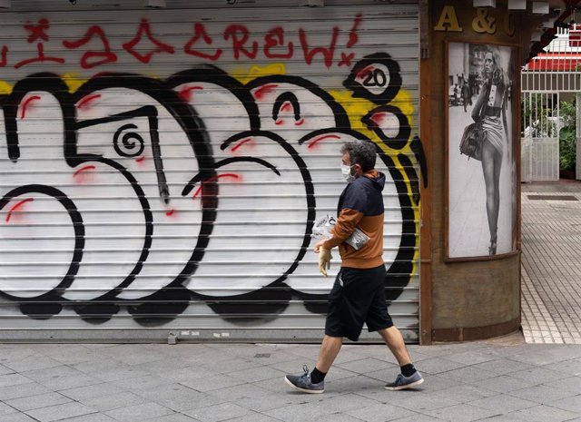 Un ciudadano pasea delante de un bar cerrado durante el estado de alarma en Sevilla