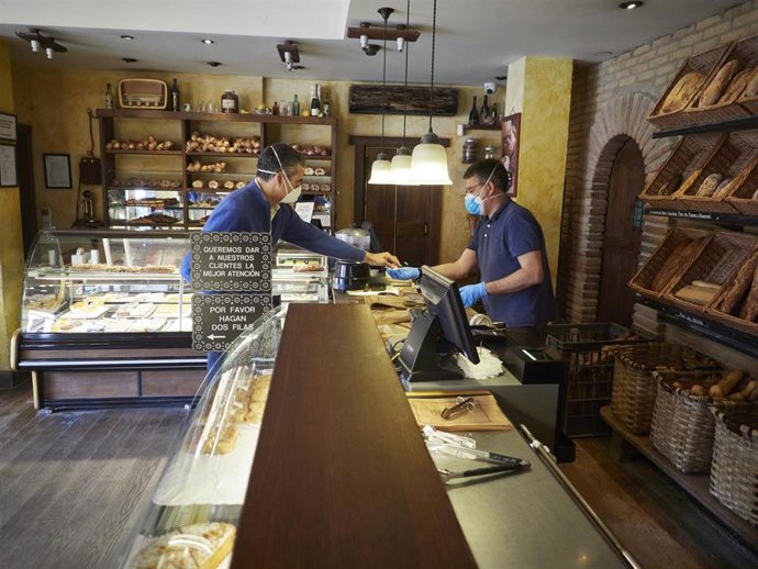Un trabajador protegido con mascarilla ofrece producto a un cliente en el obrador panadería 'Panadero de Eugui' durante en el día 32 del estado de alarma, uno de los establecimientos que puede permanecer abierto por despachar alimentos en Huarte / Navar