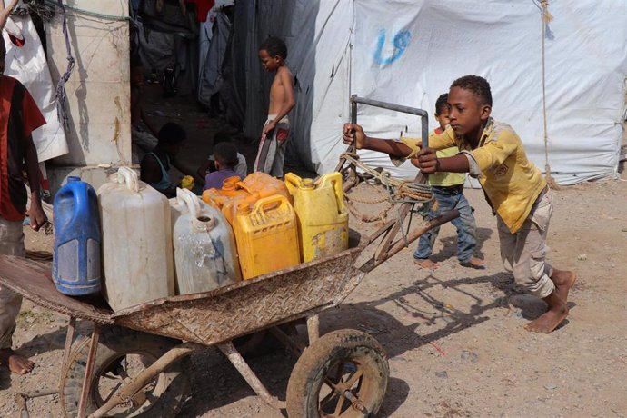 Un niño transporta una carretilla con bidones en Adén