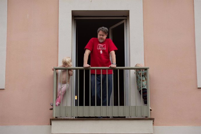 Un home i els seus dos fills petits treuen el cap a la balconada l'estat d'alarma pel coronavirus, a Barcelona.