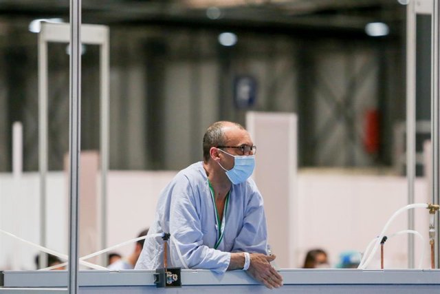 Un paciente se asoma por encima de una mampara durante la lectura de pasajes de ‘El Quijote’ para los sanitarios y pacientes del Hospital temporal de IFEMA.