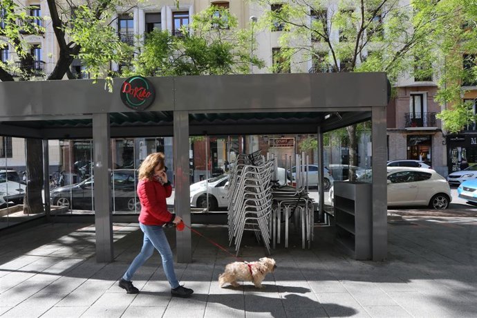 Una mujer pasa junto a una terraza cerrada de un bar en Madrid un día después de que el Gobierno presentara su plan de desescalada.