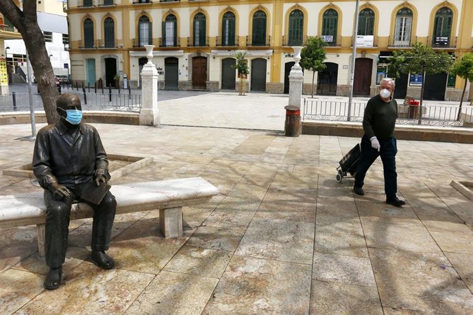 Una señor para delante de la estatua del pintor malagueño, Pablo Picasso, ubicada en la Plaza de la Merced de Málaga, ataviada con una mascarilla para protegerse del virus COVID-19. Málaga a 25 de abril del 2020
