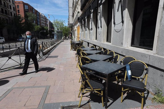 Un hombre con mascarilla pasa junto a una terraza cerrada de un bar en Madrid un día después de que el Gobierno presentara su plan de desescalada en la crisis del coronavirus y de que el sector de la hostelería se pronunciara en su contra. 