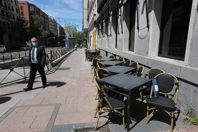 Un hombre con mascarilla pasa junto a una terraza cerrada de un bar.