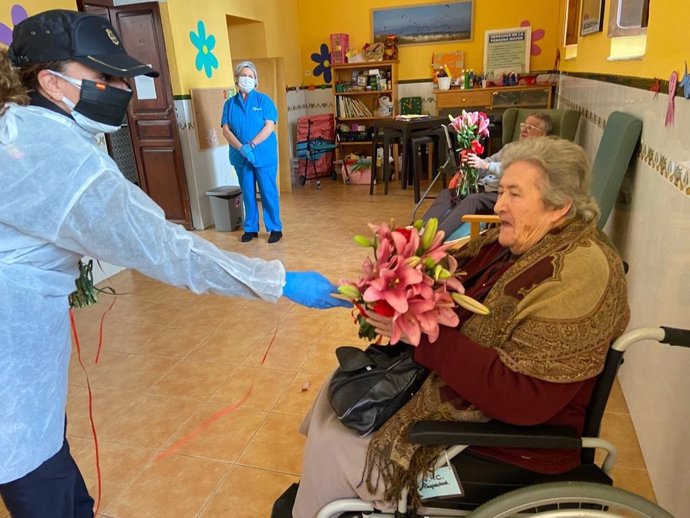 Una agente de la Policía Nacional entrega flores a una persona mayor en una residencia de Tarifa